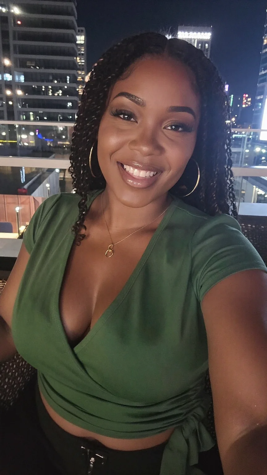 Curvy woman in green wrap top laughing on a rooftop with city lights