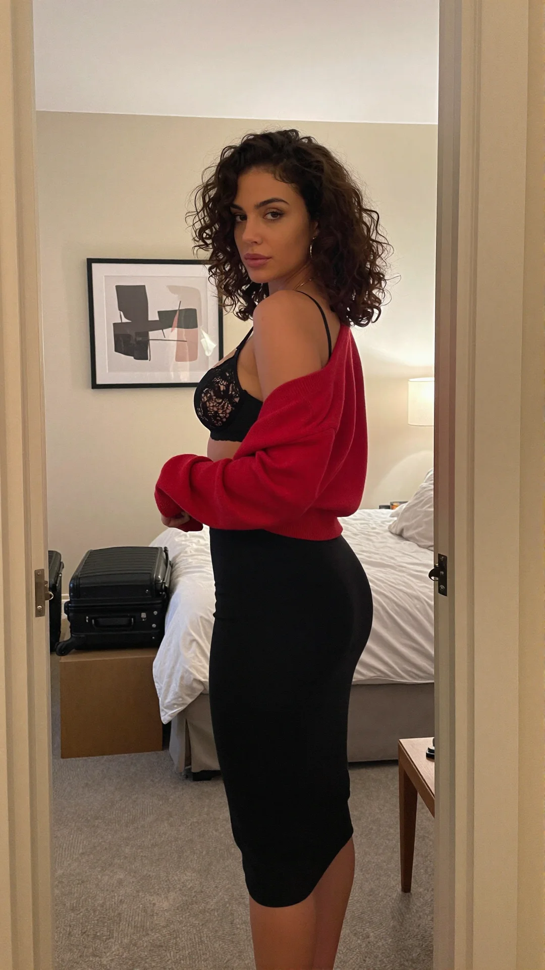 Black-haired woman in a scarlet off-shoulder dress standing in an apartment doorway
