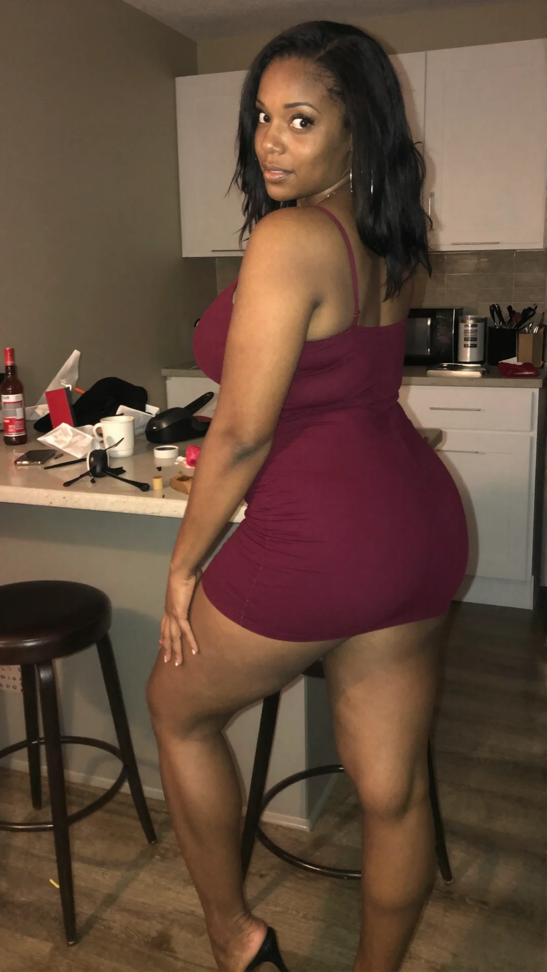 Ebony woman in burgundy fitted dress leaning at a kitchen island