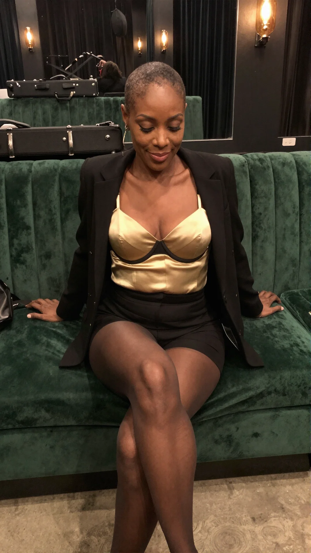 Elegant mature woman seated on a backstage greenroom sofa in gold satin and black lace